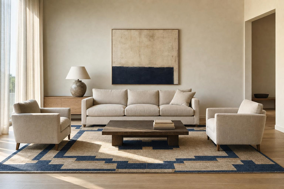 Un grand tapis à bordure bleu nuit ancre le canapé et les deux fauteuils d’un salon clair